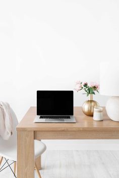 a laptop computer sitting on top of a wooden table next to a vase with flowers