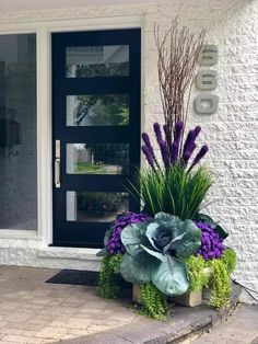 a planter with purple flowers and green plants sits on the front step of a house