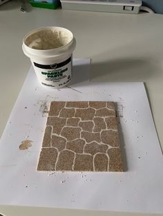 a bucket of paint sitting on top of a table next to a square shaped tile