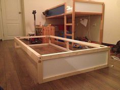 an unfinished bed frame in the middle of a living room with hard wood flooring