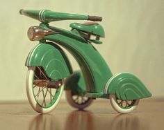 a green toy scooter sitting on top of a wooden floor next to a white wall