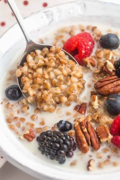 a white bowl filled with granola, berries, nuts and yogurt next to a spoon