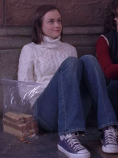 two young women sitting on the ground with their feet up and one holding a bag