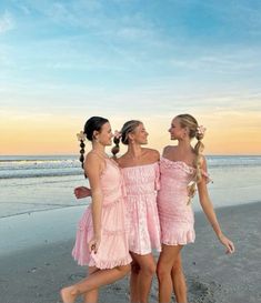 three girls in pink dresses walking on the beach at sunset with their arms around each other