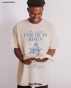 a man is reading a book and smiling at the camera while wearing a t - shirt that says, he is not there for he is risen