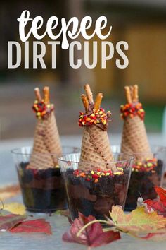 three cones with candy toppings on them are sitting in small cups, surrounded by fall leaves