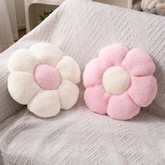 two pink and white flower pillows sitting on top of a gray bed next to each other