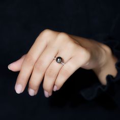 a woman's hand wearing a ring with a black pearl on it, against a black background