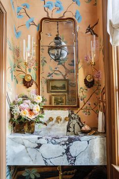 a bathroom sink sitting under a mirror next to a vase with flowers on top of it