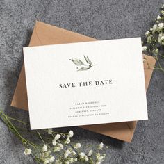 save the date card on top of an envelope next to some flowers and greenery