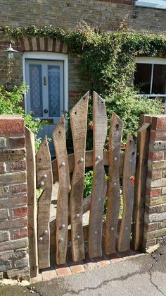 a wooden fence made out of boards and nails in front of a brick building with a blue door