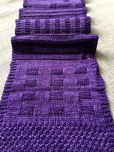 a purple knitted tie laying on top of a white bed sheet with two rows of squares