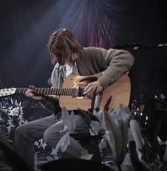 a man with long hair is playing an acoustic guitar in front of some microphones