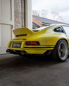 the rear end of a yellow porsche 914 parked in front of a garage door