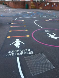 an outdoor playground with chalk drawings on the ground and words painted on the pavement that read jump over the hurdles