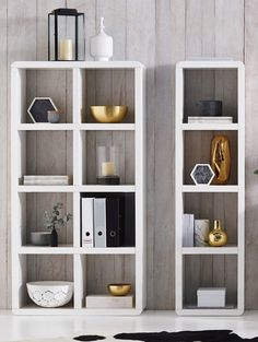 two white bookcases with books and vases on them in front of a wooden wall