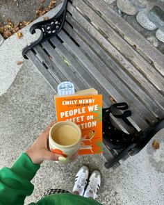 a person holding a cup of coffee in front of a bench with an orange book on it