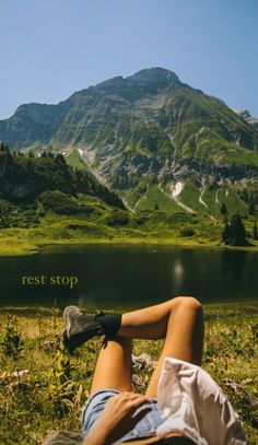 a person laying on the ground with their feet up in front of a mountain lake