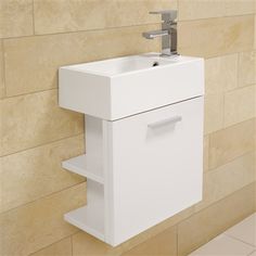 a white sink sitting next to a wall mounted faucet on a tiled wall