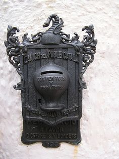 a black fire hydrant mounted to the side of a building with an ornate design