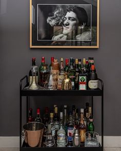 a bar cart filled with bottles and liquors in front of a framed portrait on the wall