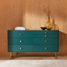 a blue dresser sitting next to a wooden wall with vases on top of it