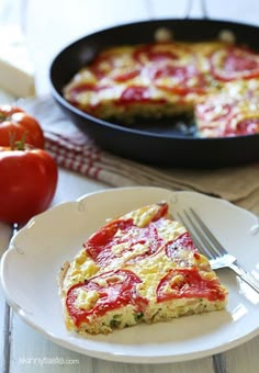 a slice of quiche on a plate next to tomatoes and a skillet with a fork