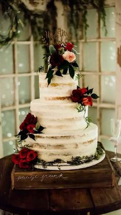 a white wedding cake with red flowers and greenery