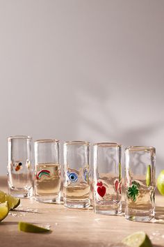 four shot glasses filled with different types of drinks on a table next to limes and an apple