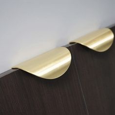 two brass curved handles on a wooden cabinet