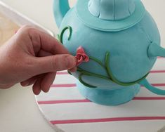 a person is placing a flower on top of a teapot