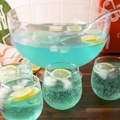 three glasses filled with blue liquid and lemon slices next to a pitcher of ice water