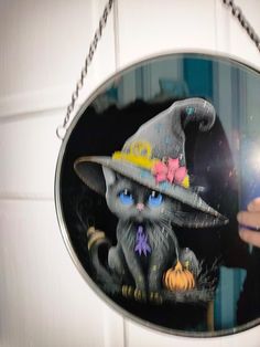 a hand holding a mirror with an image of a cat in a witches hat on it