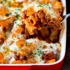 a red casserole dish filled with pasta and meat covered in sauce, cheese and parmesan