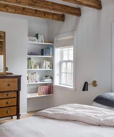 a bed sitting under a window next to a wooden dresser