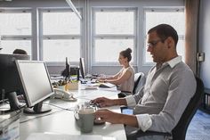 a man sitting at a desk in front of two computer monitors and a cup of coffee