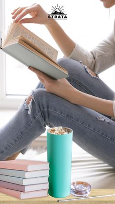 a woman sitting on the floor reading a book next to a coffee cup and stack of books