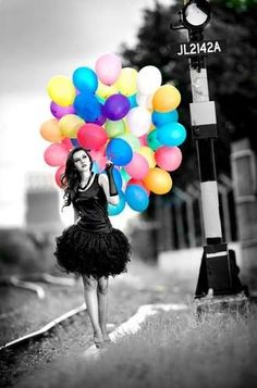 a woman is walking down the street with many balloons in her hand and she has on a black dress