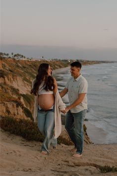 a pregnant woman holding her husband's hand on the beach