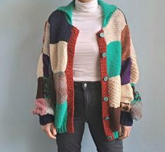 a woman standing in front of a gray wall wearing a multicolored cardigan