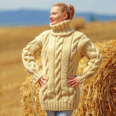 a woman standing in front of hay bales wearing a cabled sweater and jeans