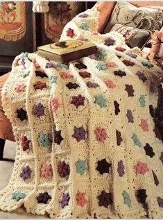 a crocheted blanket with flowers on it and a book laying on the bed