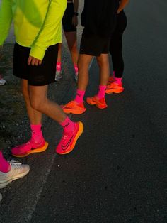 a group of people standing on the side of a road wearing neon colored running shoes