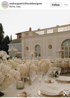 the table is set with white flowers and candles for an elegant wedding reception in front of a large building