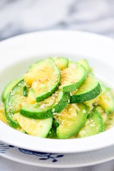 a white bowl filled with sliced cucumbers on top of a blue and white plate