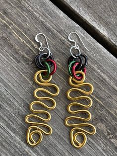 Handmade Wakanda Inspired Earrings.  Made from aluminum wire these earrings are light weight and easy to wear.   These earrings are approximately 3 inches long in a gold triangle shape with green, black, and red accents. They have sterling silver ear wire. This item is made by hand one at a time. Everything can be customized with different colored wires. There may be slight variations with each design.  Thank you for visiting my shop and supporting the art of handcrafted jewelry.  This design is Unique Black Wire Wrapped Earrings, Black Wire Wrapped Earrings, Aluminum Wire Jewelry, Afrocentric Earrings, Wire Jewellery, Gold Triangle, African Earrings, Wire Jewelry Designs, Jewellery Ideas