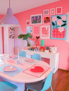 a dining room with pink walls, blue chairs and pictures on the wall above it