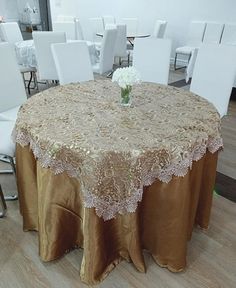 a round table covered with a brown tablecloth and white chairs in a large room