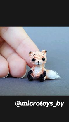 a tiny toy fox sitting on top of a persons finger in front of a gray background