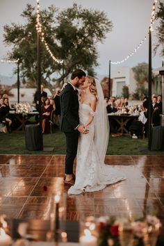 a bride and groom kissing on the dance floor in front of an outdoor wedding reception